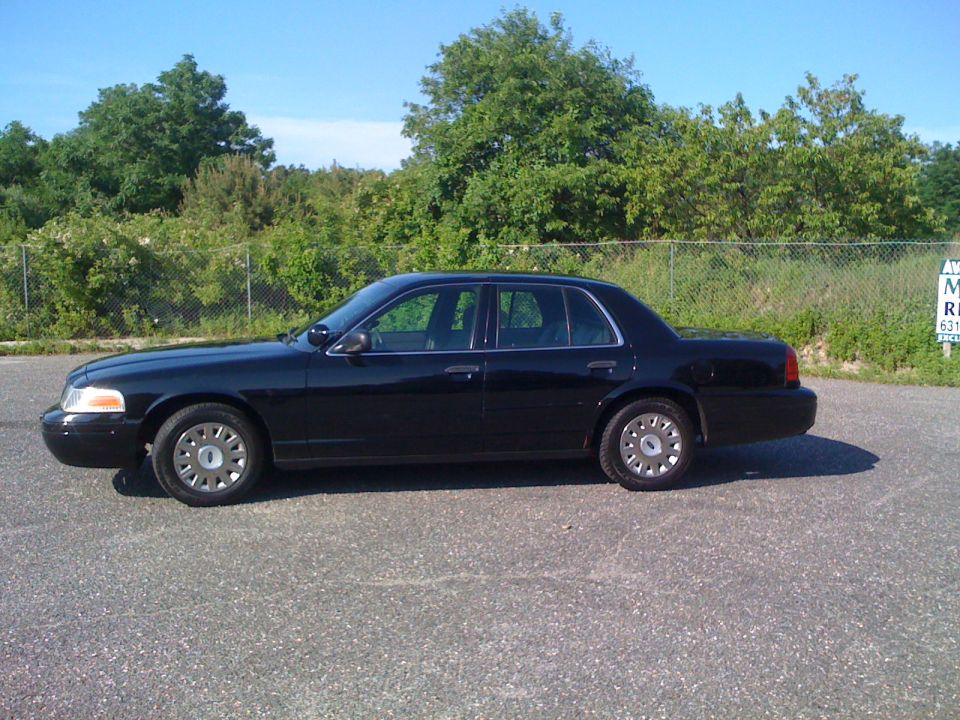 Black Ford Crown Victoria sedan in side profile on an asphalt lot