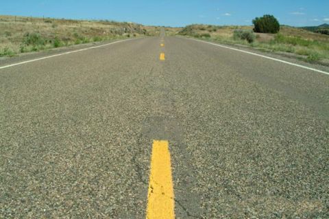 1995 Ford Bronco - An empty highway stretches towards the horizon under a clear blue sky, flanked by dry grass and hills.