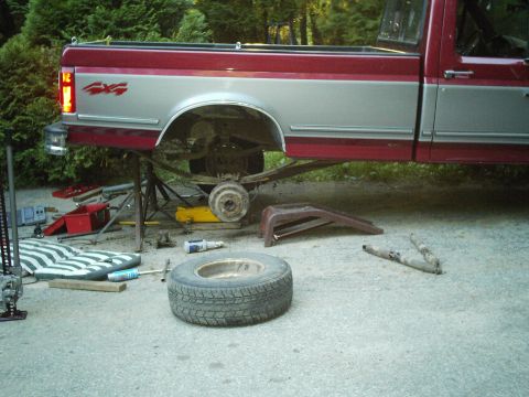 1994 Ford F-150 - The rear suspension of a pickup truck is exposed and supported by jack stands, with tools and a spare tire nearby.