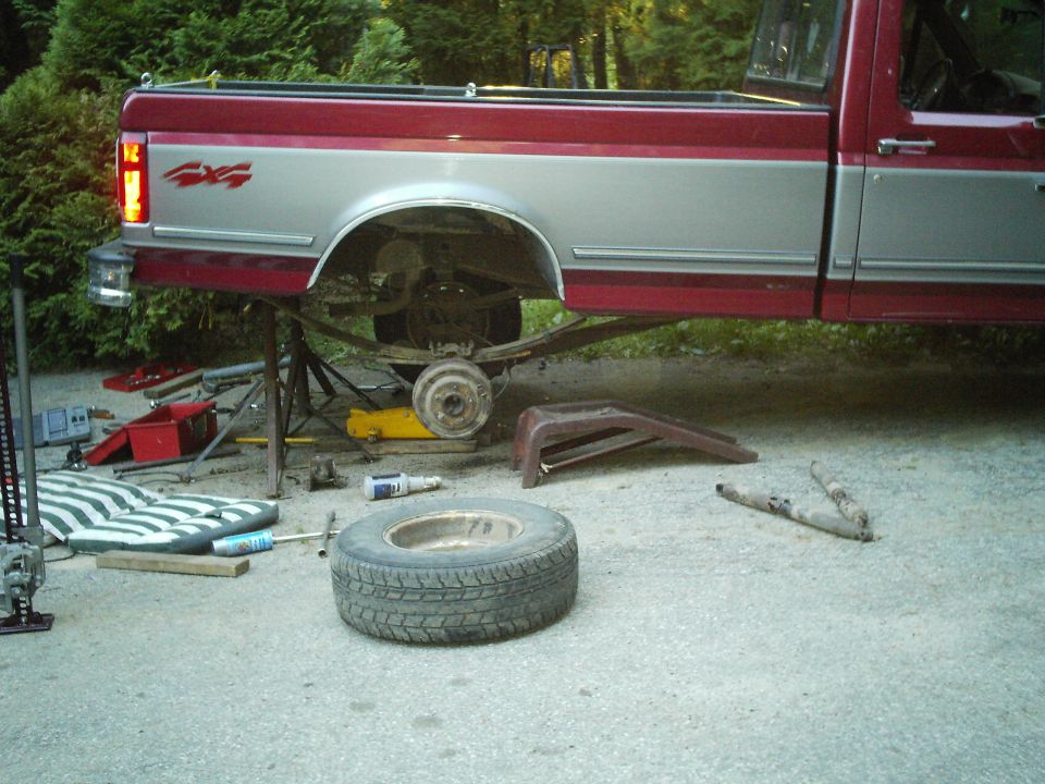 Rear of a red and silver 1994 Ford F-150 with the rear axle supported by jack stands, undergoing suspension work