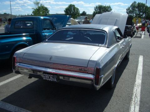 1970 Ford Mustang - This silver coupe, likely from the 1970s, is parked next to a blue pickup truck at an outdoor event.