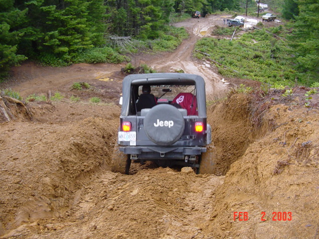Jeep Wrangler driving through mud, another vehicle visible in background