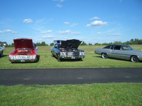 1970 Ford Mustang - A car show features several classic vehicles on a sunny day.