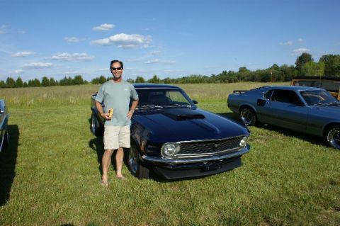 1970 Ford Mustang - A man poses with a dark blue 1970 Ford Mustang at an outdoor car show.