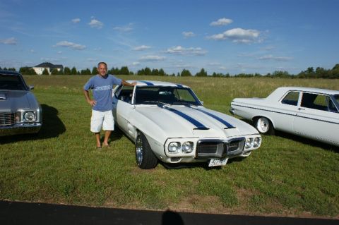 1970 Ford Mustang - A man stands next to a white 1969 Pontiac Firebird with blue racing stripes.