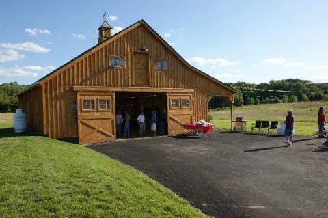 1970 Ford Mustang - A large wooden barn is the setting for an outdoor gathering on a sunny day.