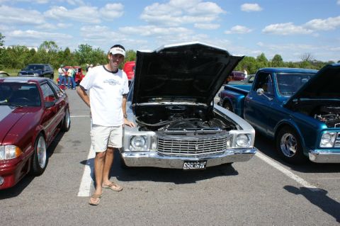 1970 Ford Mustang - A man stands next to a silver car with its hood open at an outdoor car show, with other vehicles visible in the background.