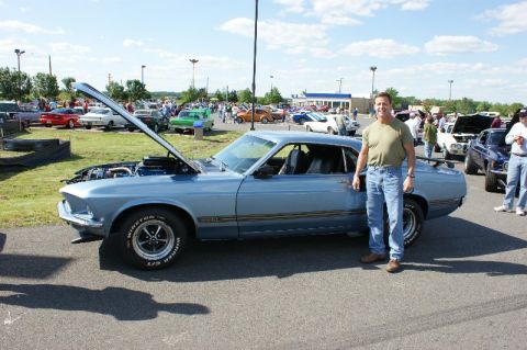 1970 Ford Mustang - A man stands next to a blue 1969 Ford Mustang coupe with its hood open at an outdoor car show.