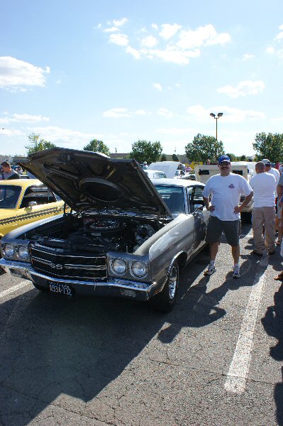 1970 Ford Mustang - A man poses with a classic Chevrolet Chevelle SS at an outdoor car show, its engine compartment displayed.