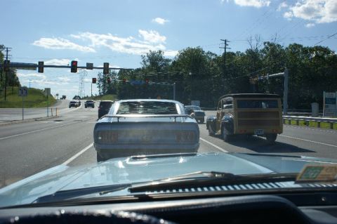 1970 Ford Mustang - A classic Mustang leads traffic on a bright day, passing a vintage woodie wagon.
