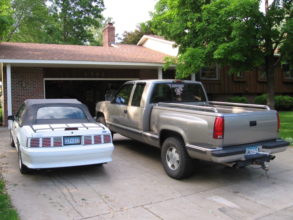 White convertible Mustang and silver pickup truck parked in a driveway.