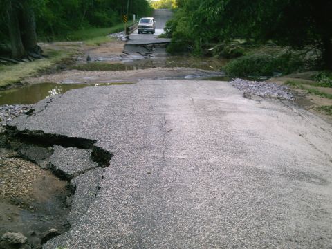 2001 Dodge 2500 - A silver van drives over a severely damaged road and bridge, likely due to flooding.