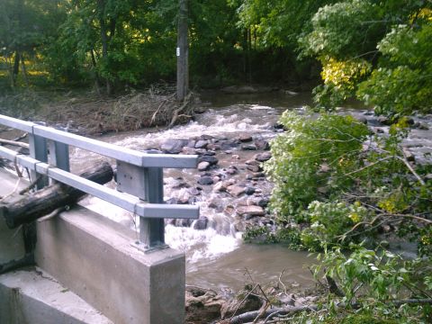 2001 Dodge 2500 - A creek flows rapidly over rocks, with debris washed up on the banks and a bridge railing in the foreground.