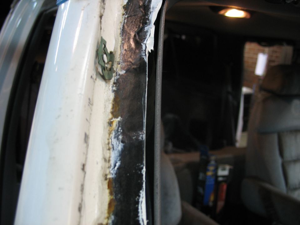 Interior door frame of a white van with rust and adhesive residue.