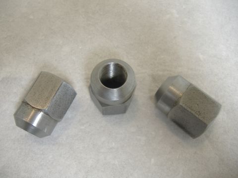1996 Ford Bronco - Three metal lug nuts are displayed on a textured surface, likely for automotive use.