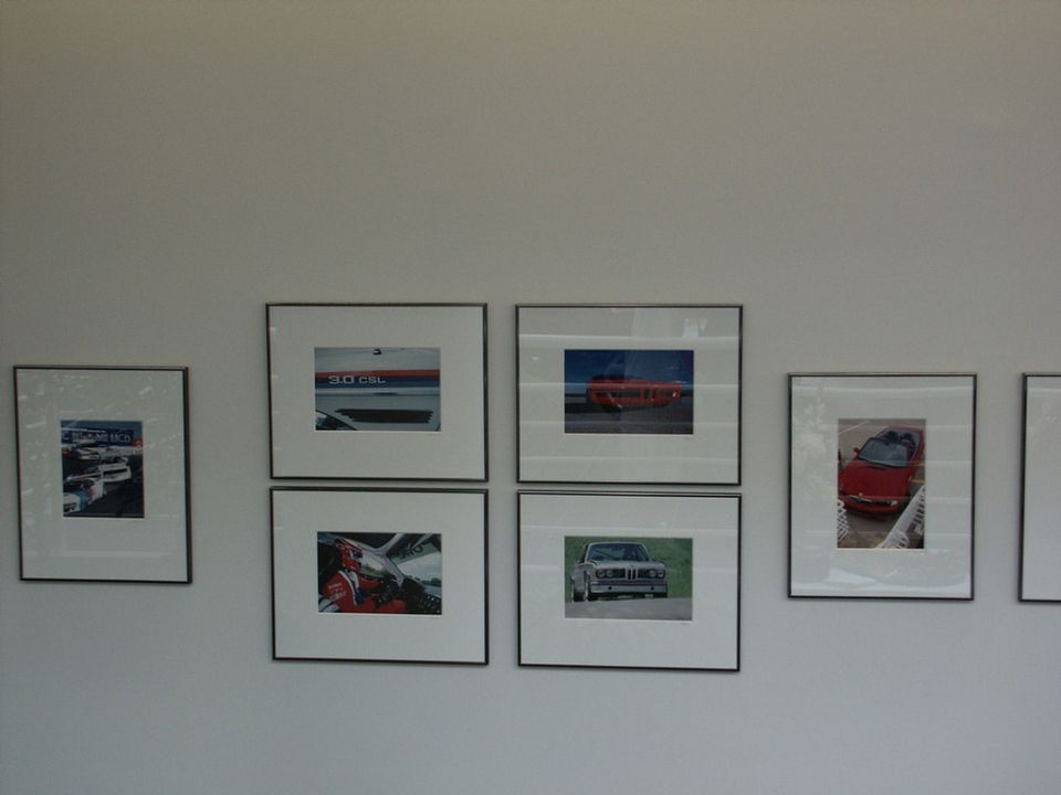 Several framed photos of cars and car parts displayed on a white wall