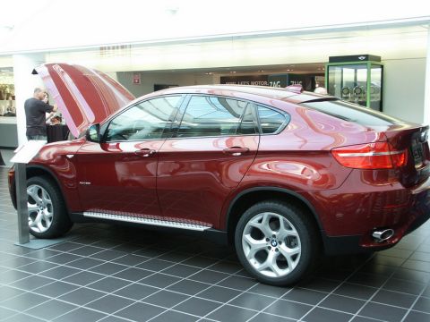 2001 Mercury Grand Marquis - A red BMW X6 is displayed indoors with its hood up, showing a person looking at the engine.