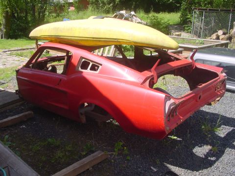 1979 Ford Bronco - A red 1967 Ford Mustang fastback body shell sits outdoors with a yellow kayak strapped to its roof.
