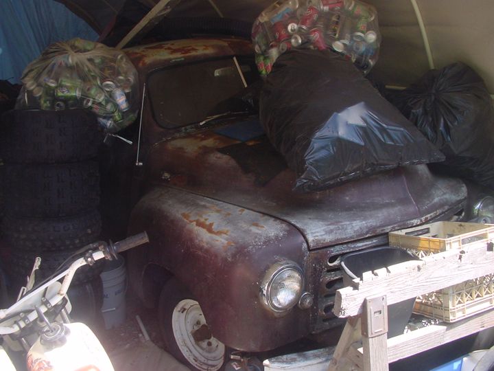 old rusty car in a garage with bags of trash and tires