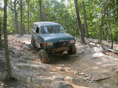 1990 Ford Bronco - This 1990 Ford Bronco tackles a challenging, rocky terrain in a wooded area.
