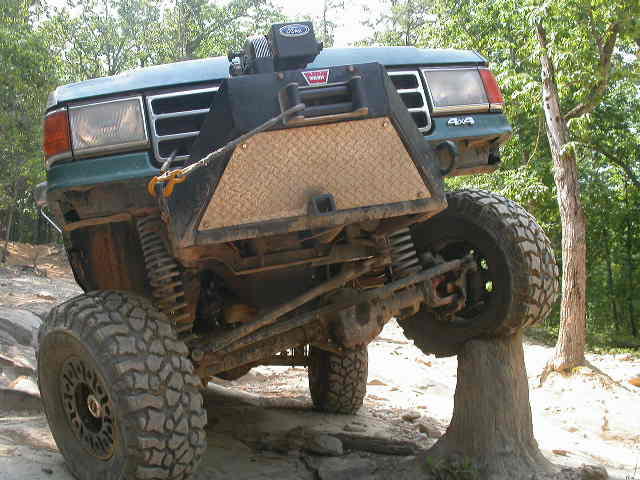 1990 Ford Bronco with aftermarket bumper and winch, climbing over a rock