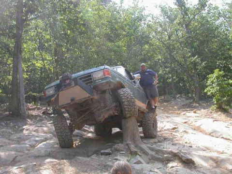 1990 Ford Bronco - A modified green SUV navigates a challenging rocky terrain with a person standing on its side.