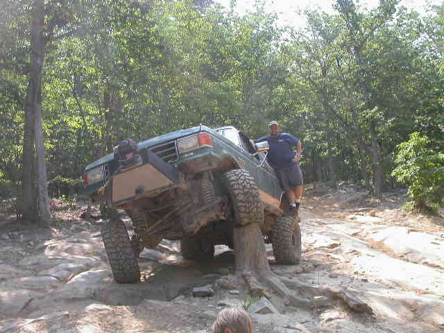 Green SUV with large tires on a rocky trail, front bumper modified with a winch