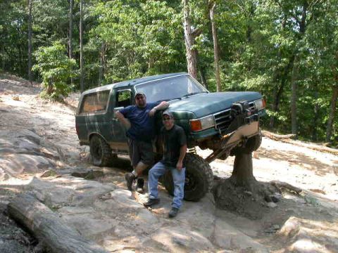 1990 Ford Bronco - Two men pose with a 1990 Ford Bronco during an off-road excursion on a dirt and rock path.