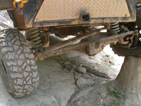 1990 Ford Bronco - The rear axle and suspension of an off-road vehicle are shown in detail, with one tire elevated on a rock.