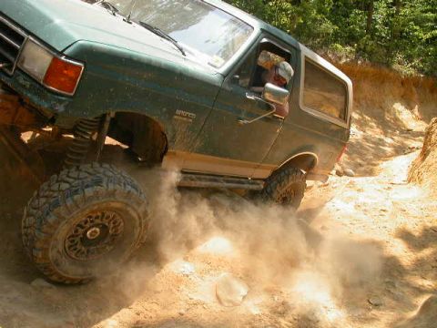 1990 Ford Bronco - A green Ford Bronco navigates a dusty off-road trail.