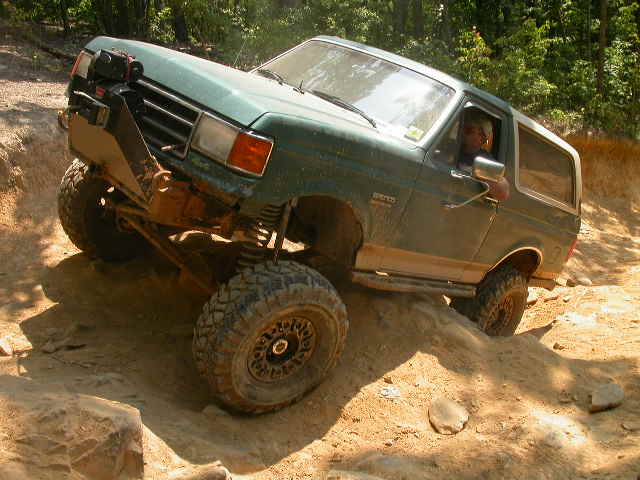 Green 1990 Ford Bronco off-roading on a dirt trail