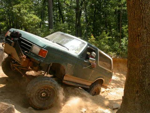 1990 Ford Bronco - This 1990 Ford Bronco is navigating a challenging off-road trail in a wooded area.