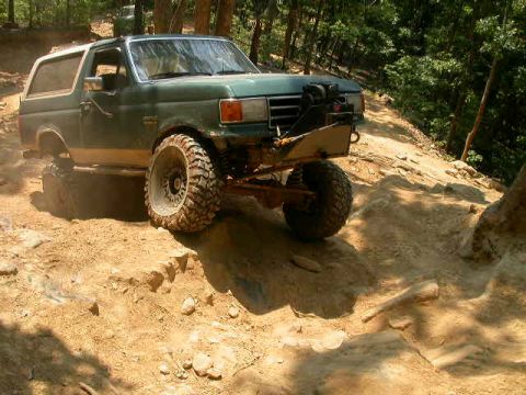 1990 Ford Bronco - A modified Ford Bronco navigates a challenging off-road trail with steep inclines and rocky terrain.