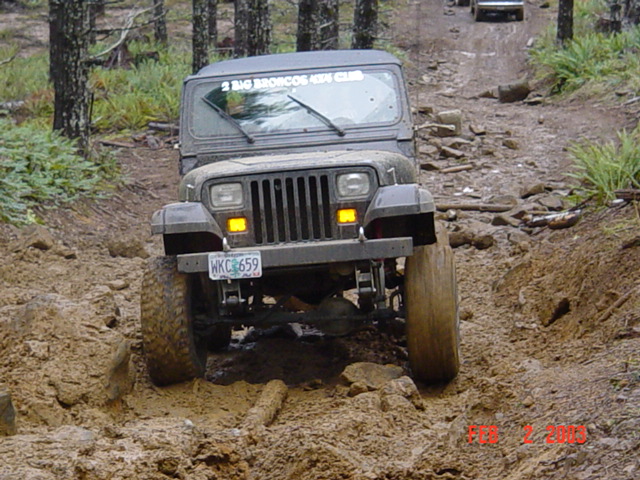 Dark gray Jeep Wrangler driving on a muddy, rocky trail. License plate WKC 659