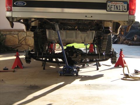 1996 Ford Bronco - The rear suspension of a 1996 Ford Bronco is elevated on jack stands for maintenance, with a floor jack positioned underneath.