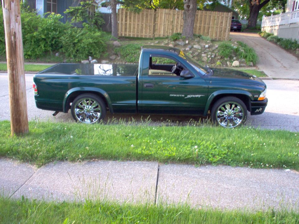 Green Dodge Dakota Sport pickup truck with chrome rims parked on a residential street