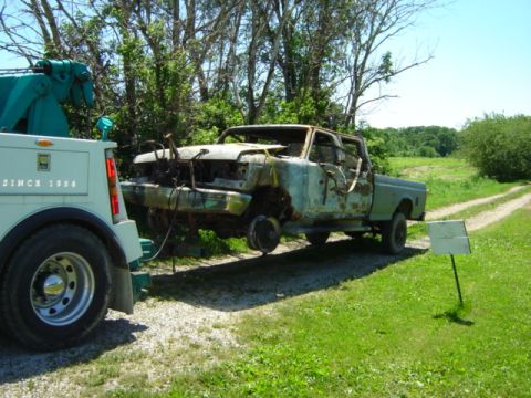 1992 Ford Bronco - A tow truck is hauling a severely damaged pickup truck on a dirt road.