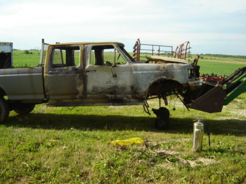 1992 Ford Bronco - A severely damaged pickup truck is being moved by a loader, with a fire extinguisher nearby.