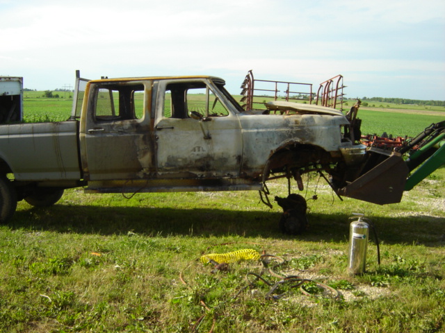 burnt pickup truck being lifted by a loader, fire extinguisher on ground