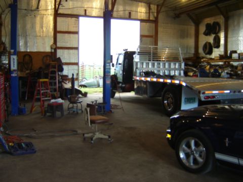 1992 Ford Bronco - A flatbed tow truck and a black car are parked inside a garage with tools and equipment around.