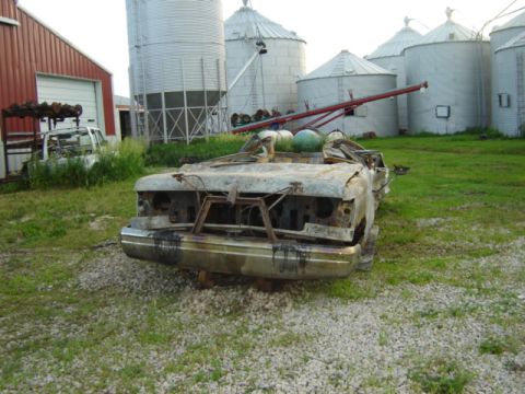 1992 Ford Bronco - Front view of a heavily damaged pickup truck, possibly from the early 1990s, with farm silos behind it.