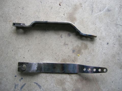 1996 Ford Bronco - Two metal linkage components are shown on a concrete surface, possibly for automotive repair or modification.