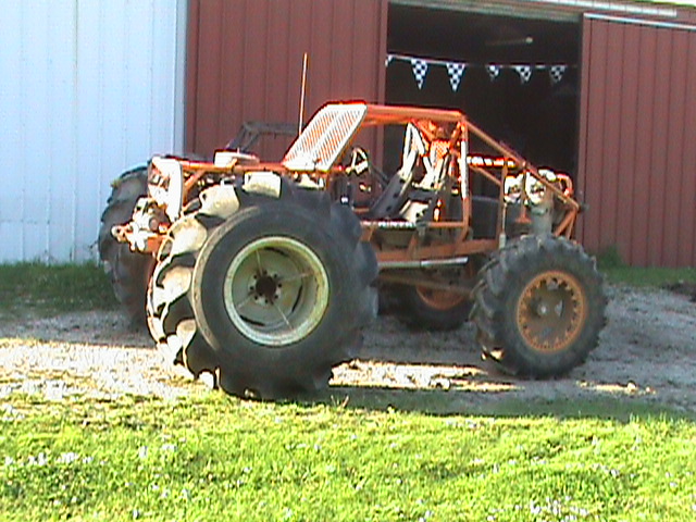 Orange custom buggy with large tires parked in front of a barn