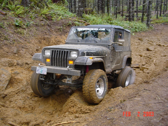 Black 1995 Jeep Wrangler navigating a steep, muddy off-road trail