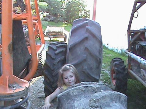 1973 Ford Bronco - A young girl is partially hidden behind a large tire, with other off-road vehicles visible in the background.
