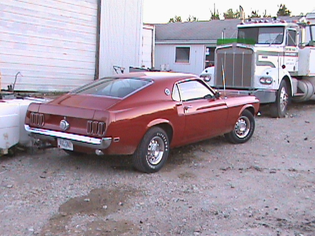 Red 1969 Ford Mustang parked next to a semi-truck