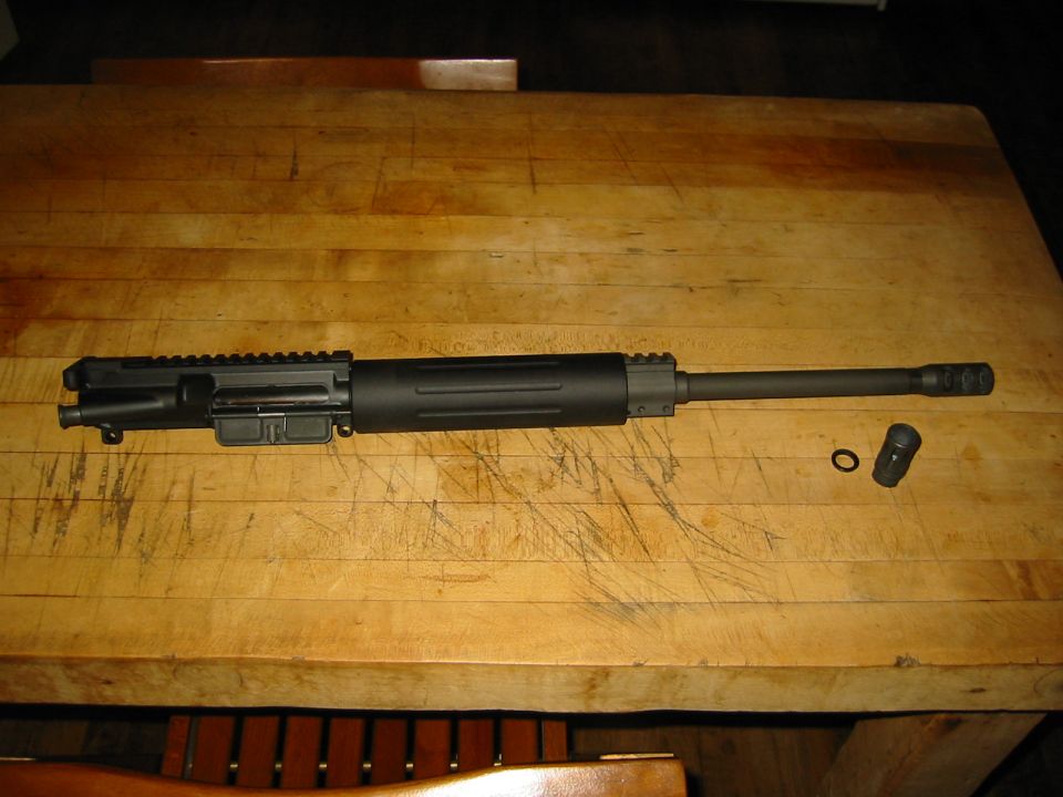 AR-15 upper receiver assembly with barrel and muzzle brake, lying on a wooden table