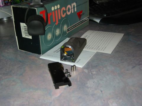 1996 Ford Bronco - Trijicon optic and its original packaging are laid out on a textured surface.