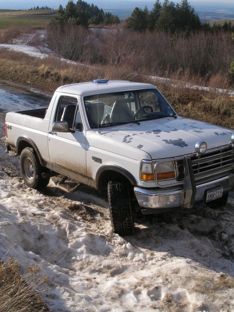 1992 Ford Bronco - A white Ford Bronco navigates a challenging snowy and muddy terrain.