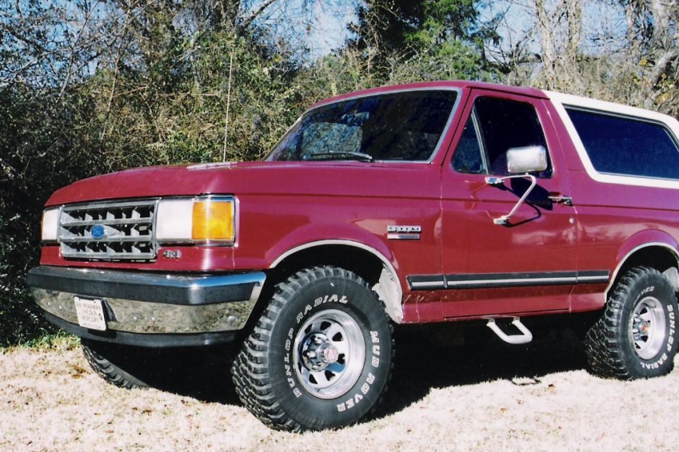 Maroon Ford Bronco with white top, off-road tires, and side steps parked outdoors